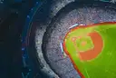Looking down into a full baseball stadium at night, with the diamond, the red-brown infield and the packed stands in view.