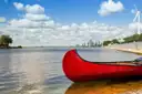 A red canoe on calm water, with a city skyline far across the lake
