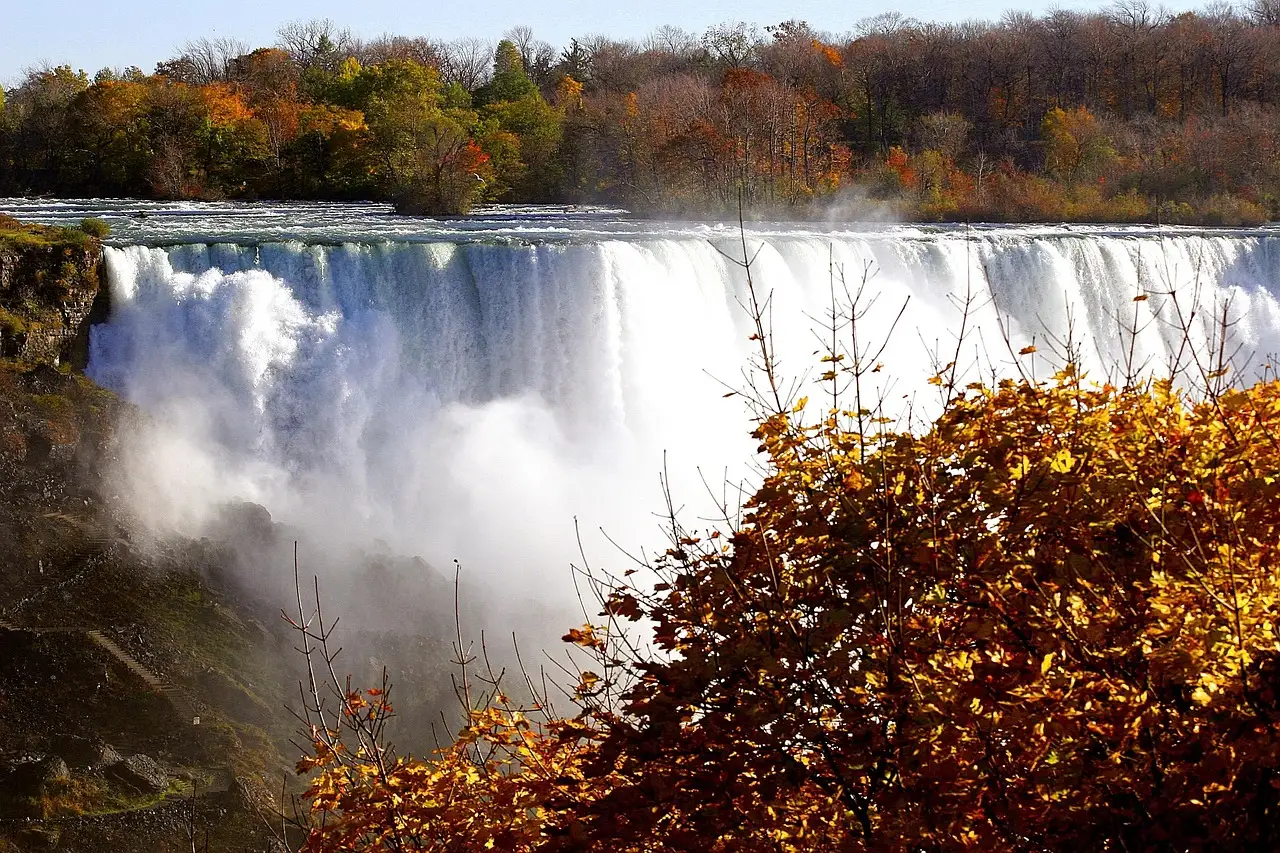 Niagara Falls throwing white spray beneath a bank of red and gold autumn leaves.