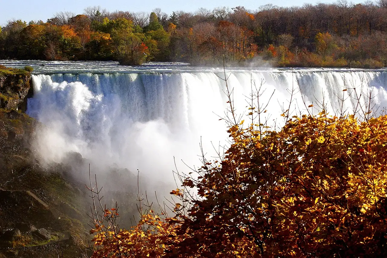 Niagara Falls throwing white spray beneath a bank of red and gold autumn leaves.