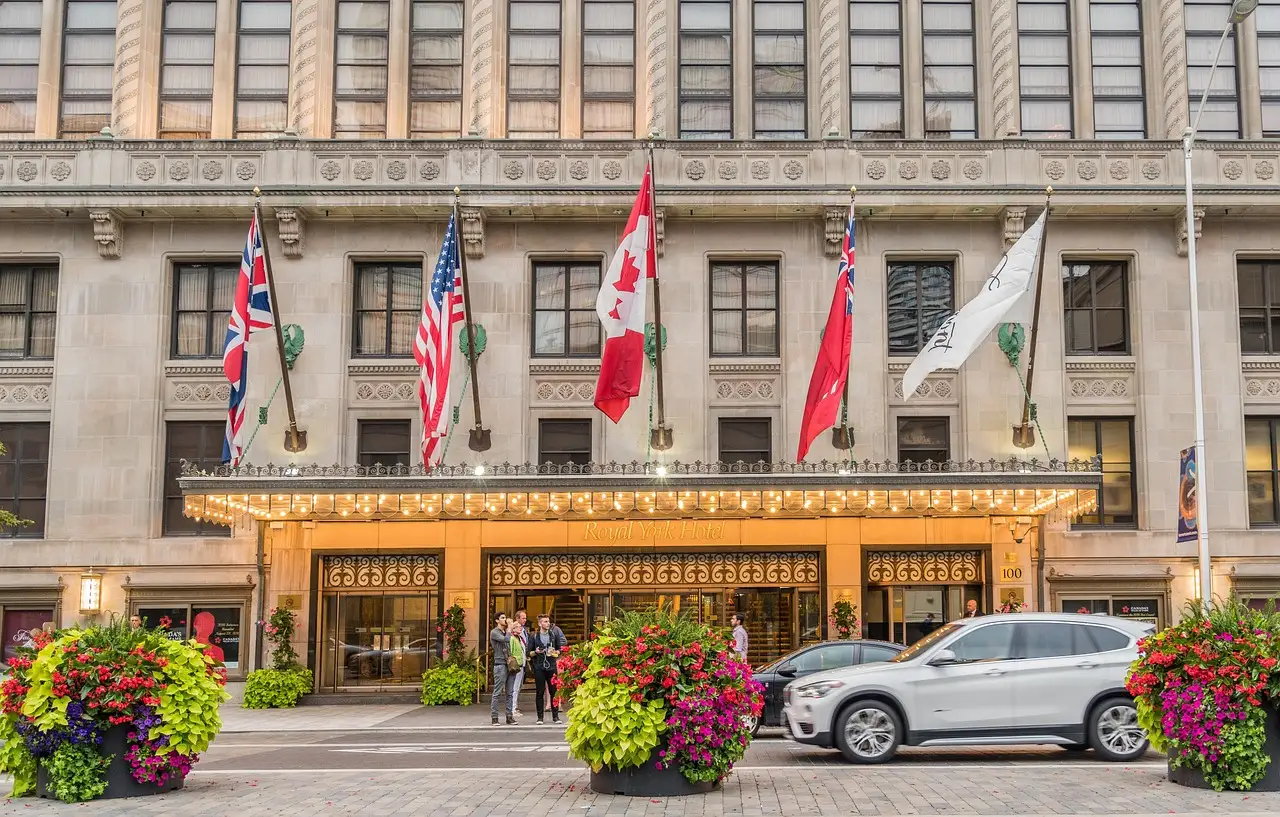 The stone front of the Royal York hotel on Front Street with flags and a lit entrance canopy, with flower planters in front.