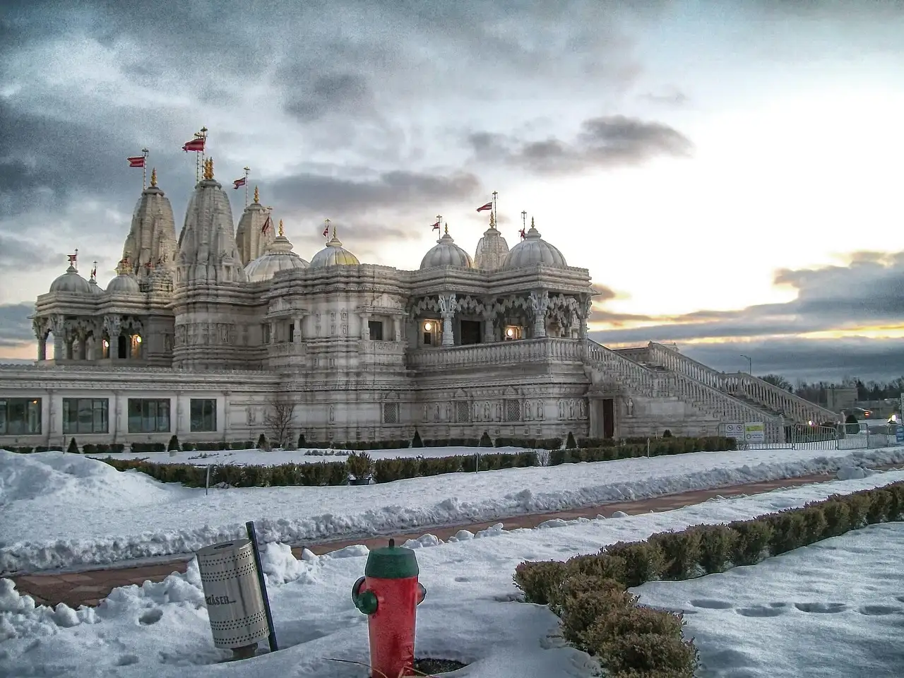 The white marble BAPS Shri Swaminarayan Mandir in Toronto at dusk, with snow on the lawn and a red fire hydrant in front.