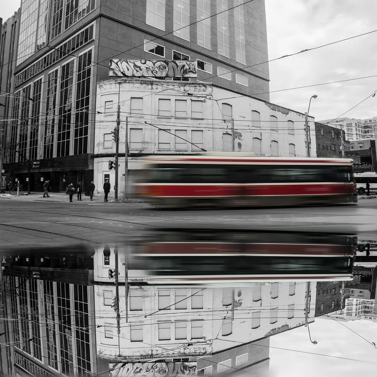 A red and white Toronto streetcar passing in motion blur on a downtown street, with its reflection in a puddle below.
