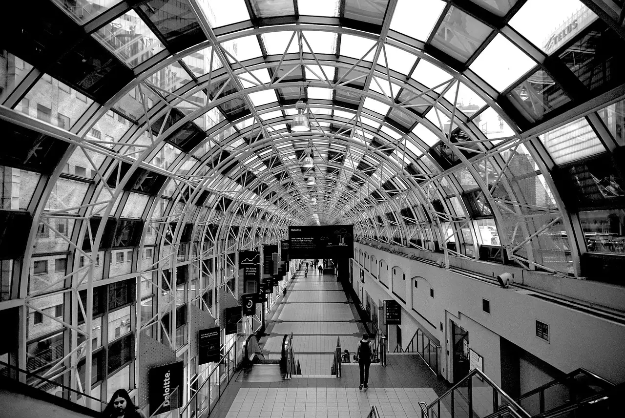 The inside of a long glass-roofed station walkway in Toronto in black and white, with a few commuters far down it.