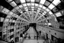 The inside of a long glass-roofed station walkway in Toronto in black and white, with a few commuters far down it.